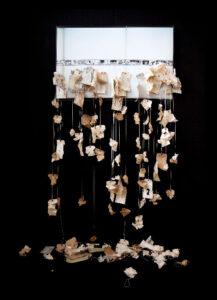 Suspended torn paper installation on black background.