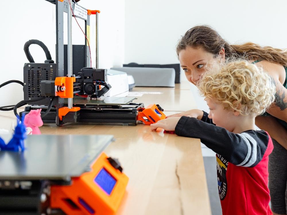 adult showing kid 3d printer Child and adult exploring 3D printer interaction.