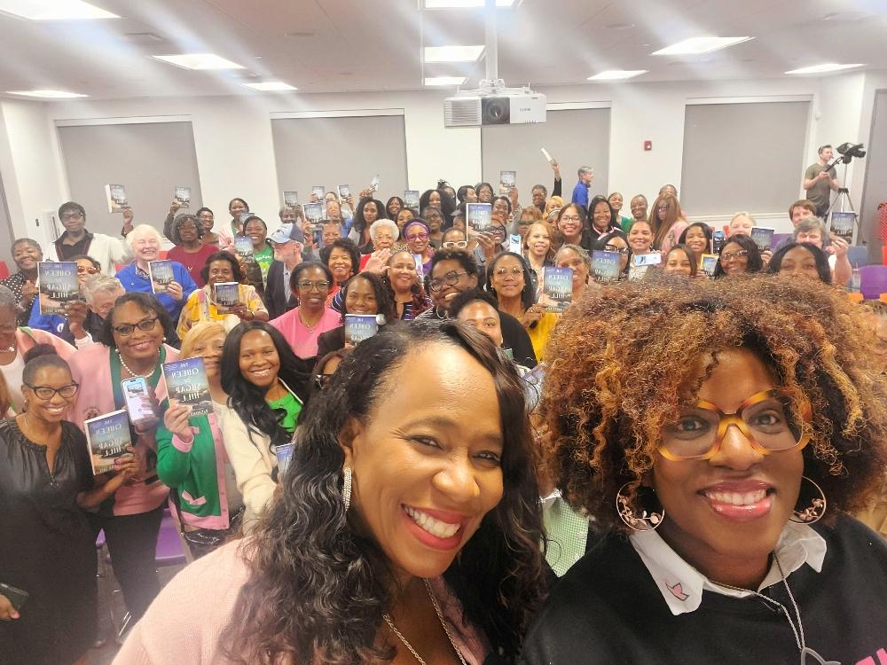 Group of smiling people holding books at an event.