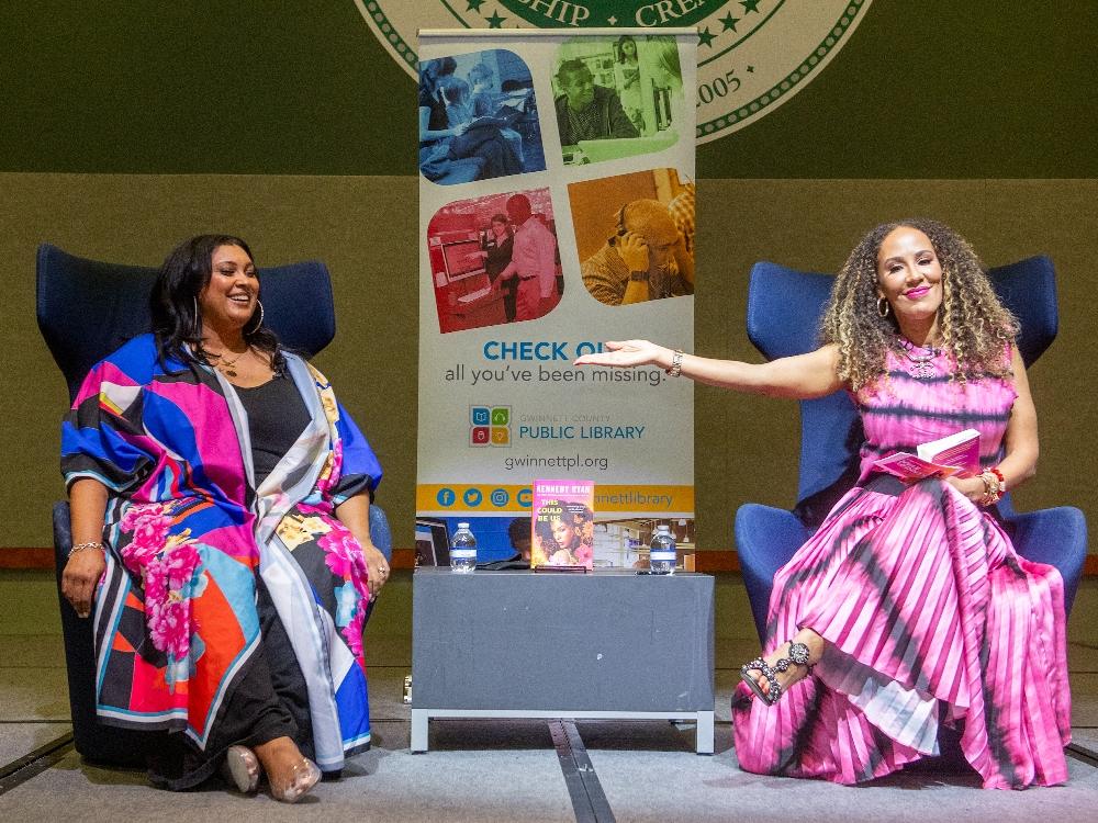Two women speaking at library event with banner.