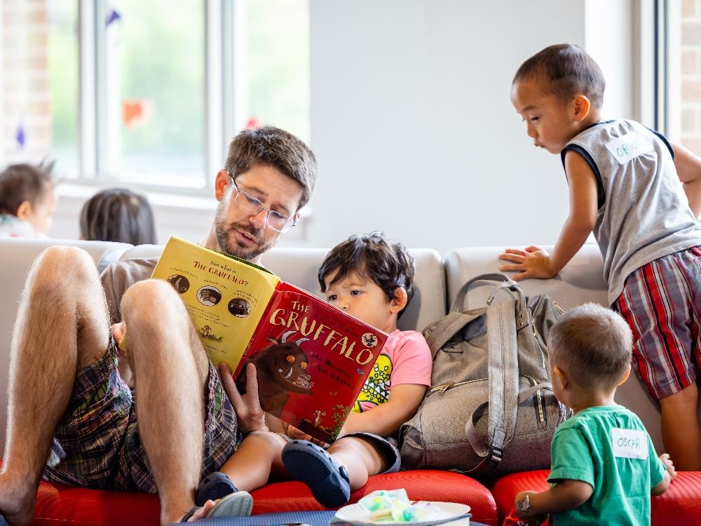 early childhood literacy 3 Man reading book with children on a couch.
