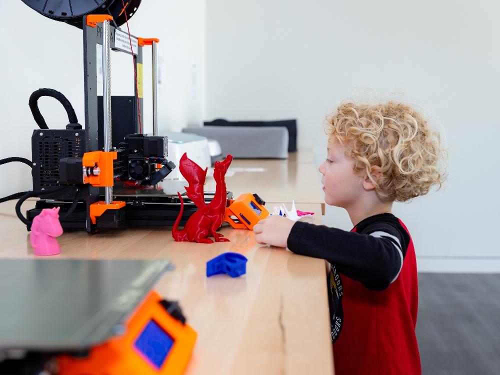 Child playing with 3D printer and colorful models.