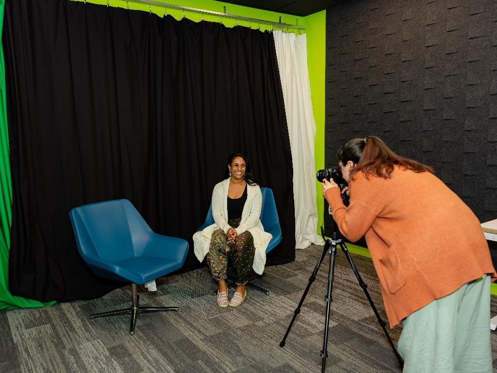Photographer taking portrait of seated woman in studio.