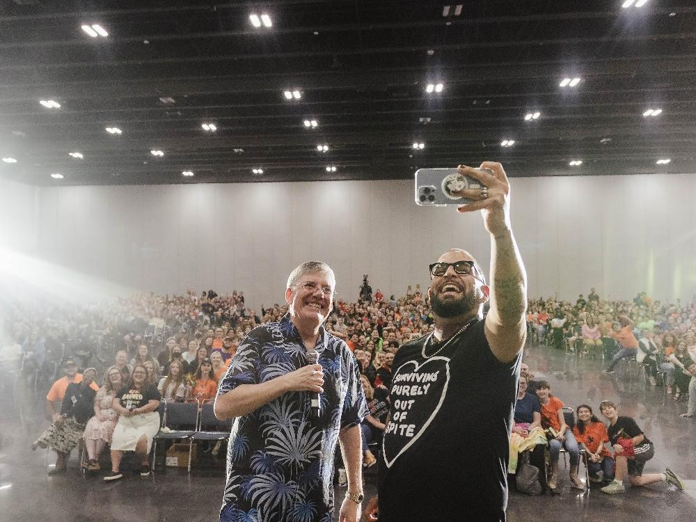 Two men taking selfie with large audience.