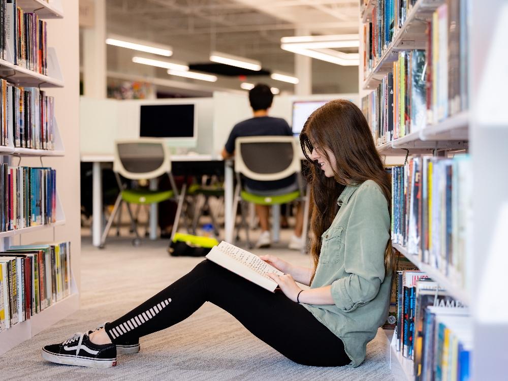 teens teen reading in a library Person reading book in library aisle.