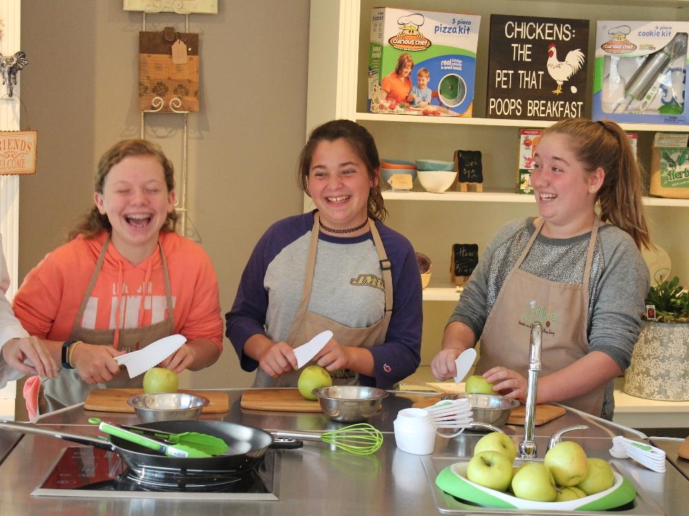 Kids laughing while preparing apples in kitchen class.