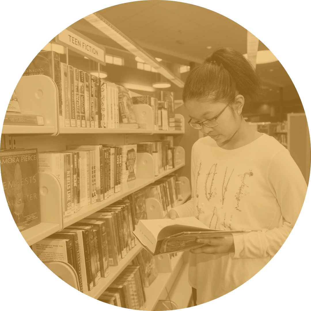 Teen reading a book in library teen fiction section.