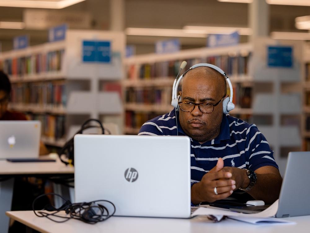 welcoming spaces for tech work 6 Man in library using laptop and headphones.