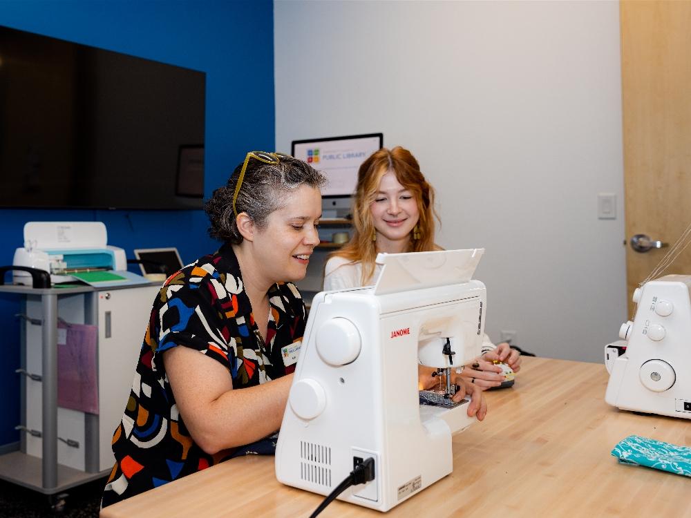 Two people sewing in a classroom setting.