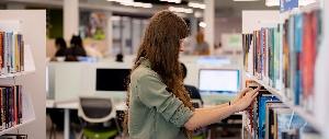 Woman browsing library books on shelves.