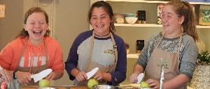 Three girls laughing and peeling apples in kitchen.