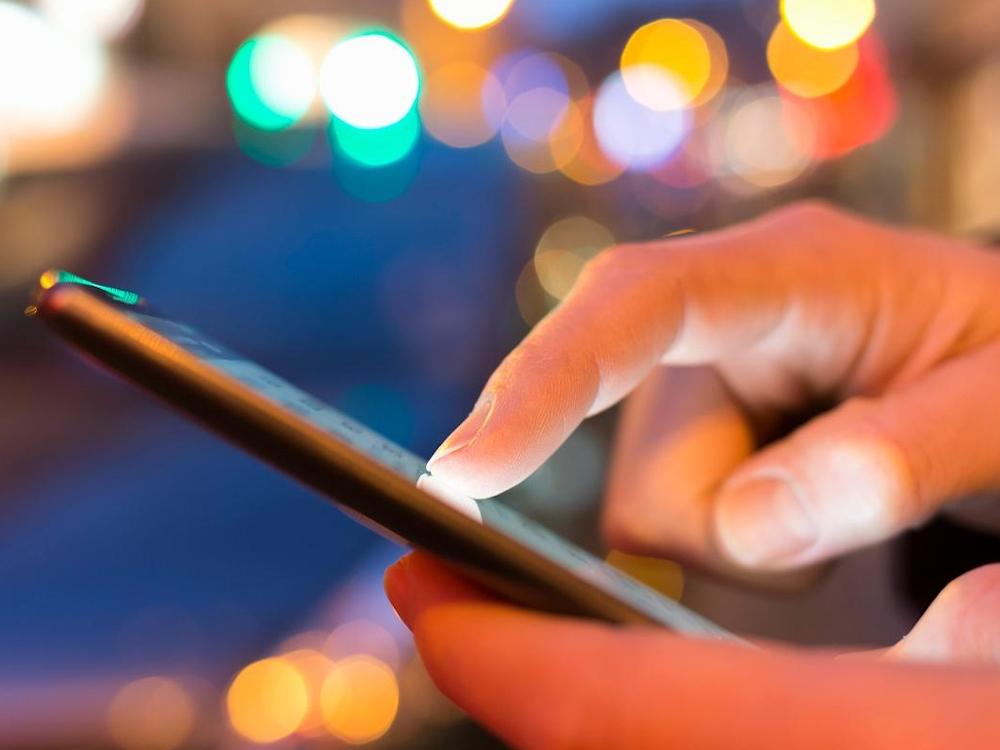 Person using smartphone with colorful lights background.