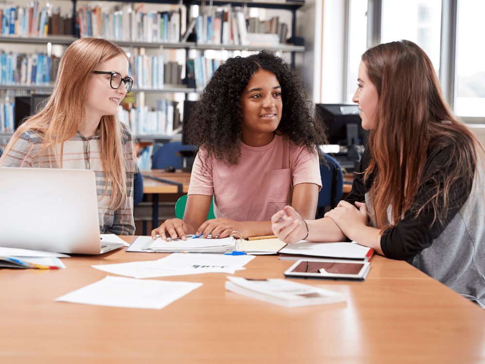 photo of teens studying Students collaborating in a library with laptops.