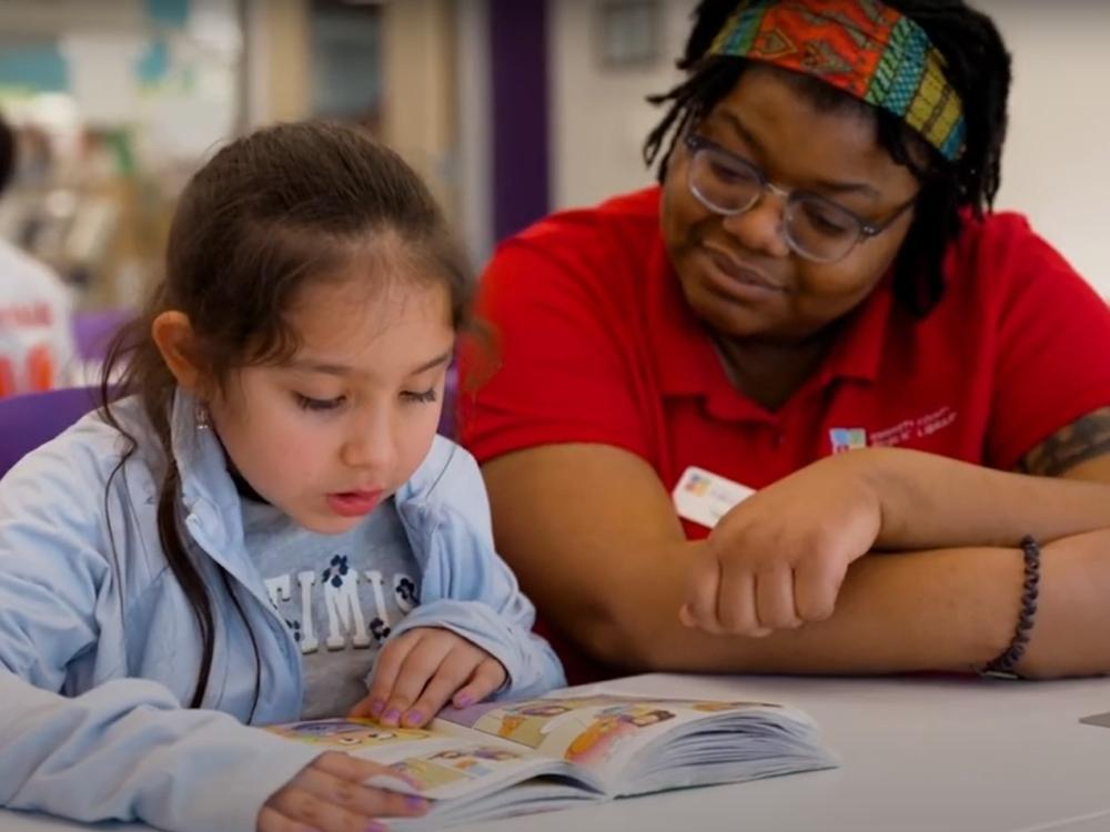 reading buddies 2 Child reading with teacher at library table.