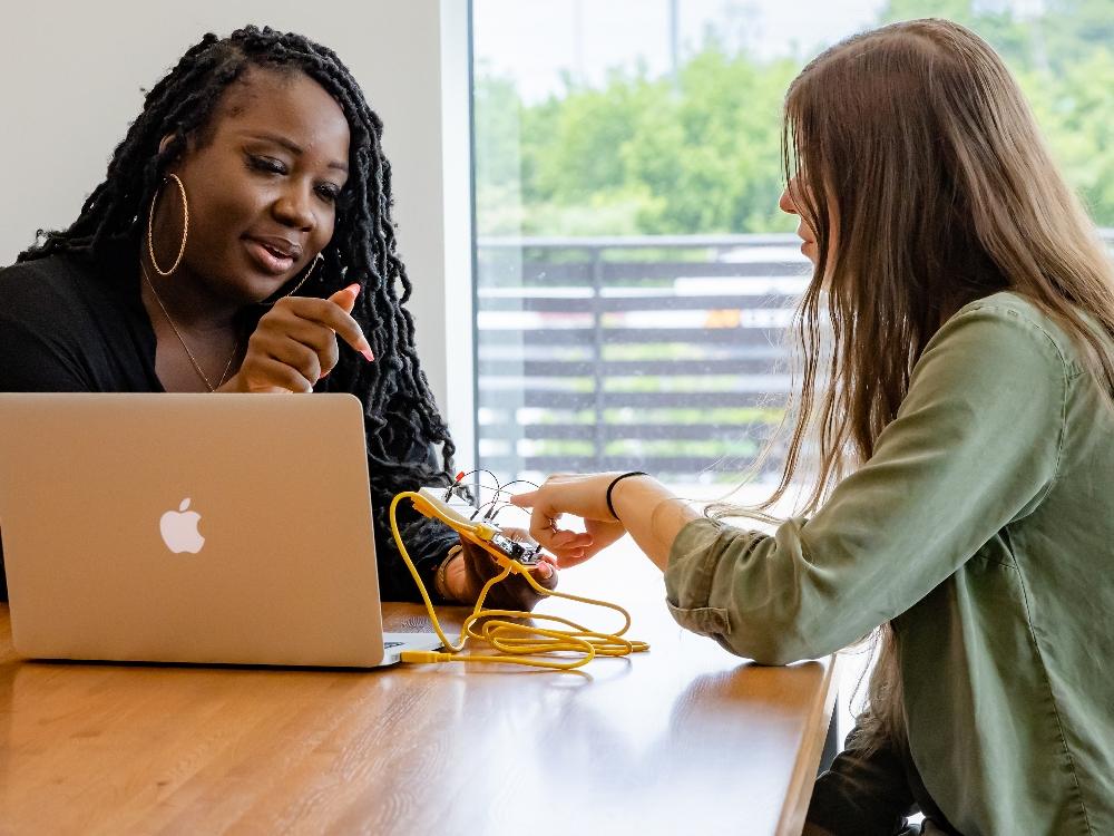 Two women discussing electronics project with laptop.