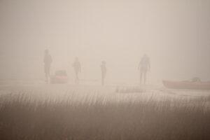 People with kayaks in dense fog on the shore.
