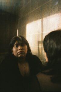 Woman reflected in mirror with sunlight on wall.