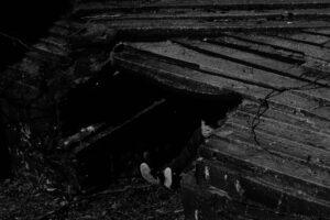 Person hiding under concrete structure in shadow.