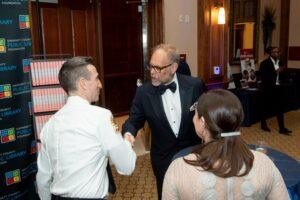 Man in tuxedo shakes hands with uniformed fire official