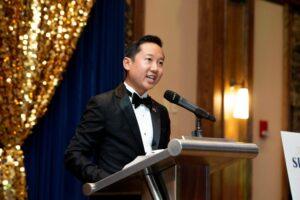 Man in tuxedo speaking at a podium microphone