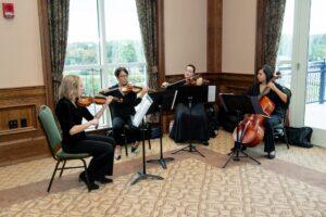 String quartet performs indoors beside large windows.